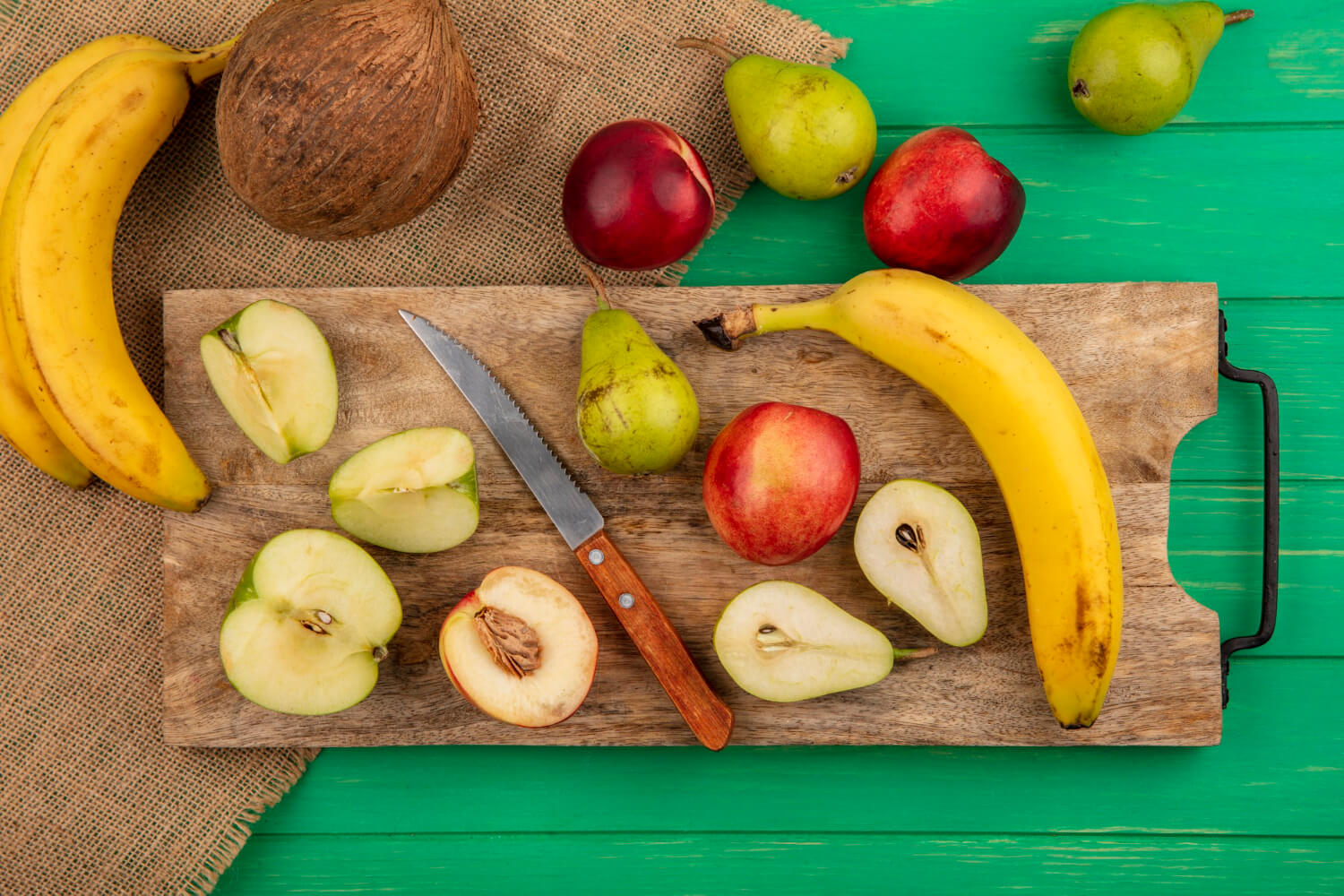 vista-superior-frutas-enteras-medio-cortadas-como-pera-manzana-melocoton-platano-cuchillo-tabla-cortar-platano-coco-sobre-tela-saco-fondo-verde